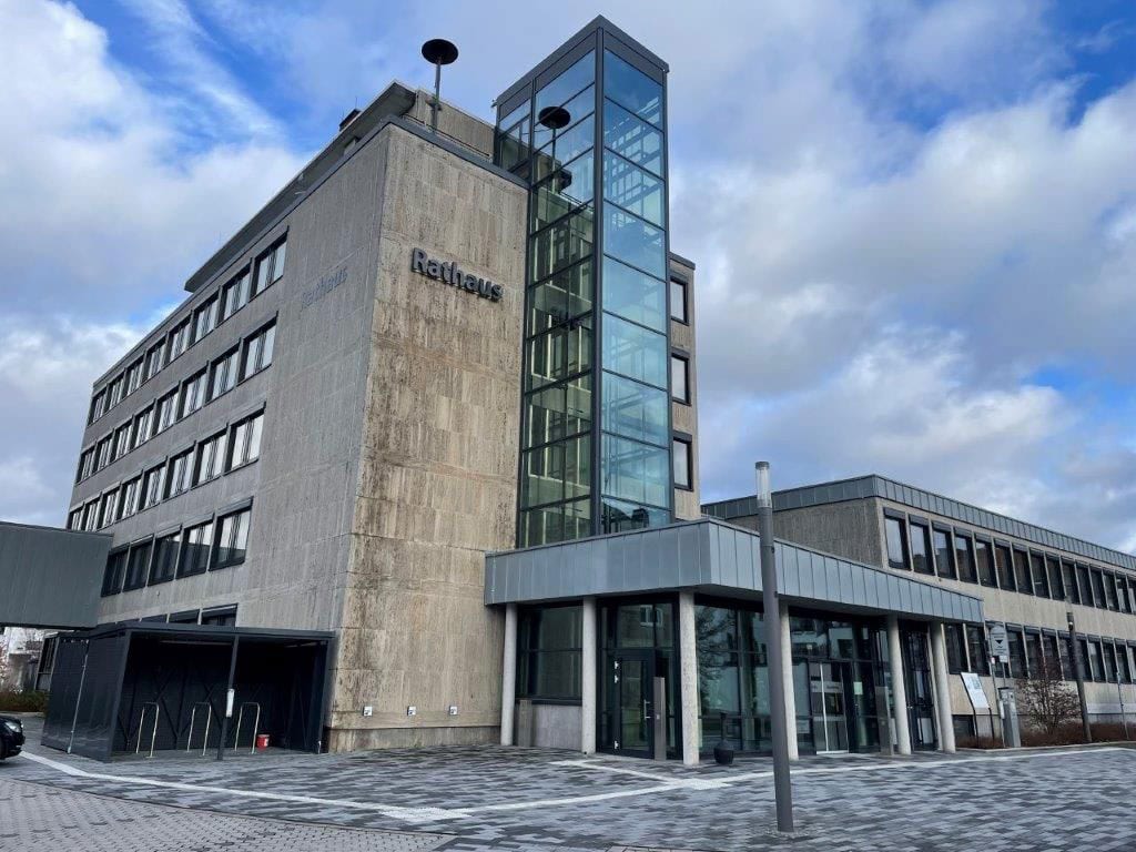 Moderne graues Gebäude unter bewölktem Himmel, markiert mit "Rathaus", mit Glasaufzug.