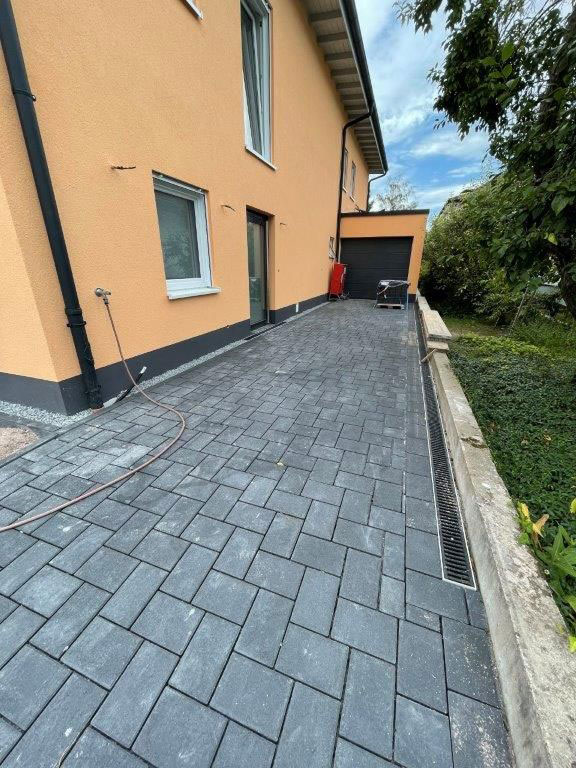 Orange Hausfassade mit grauem Pflaster, Blick Richtung Garage; Garten im Hintergrund.