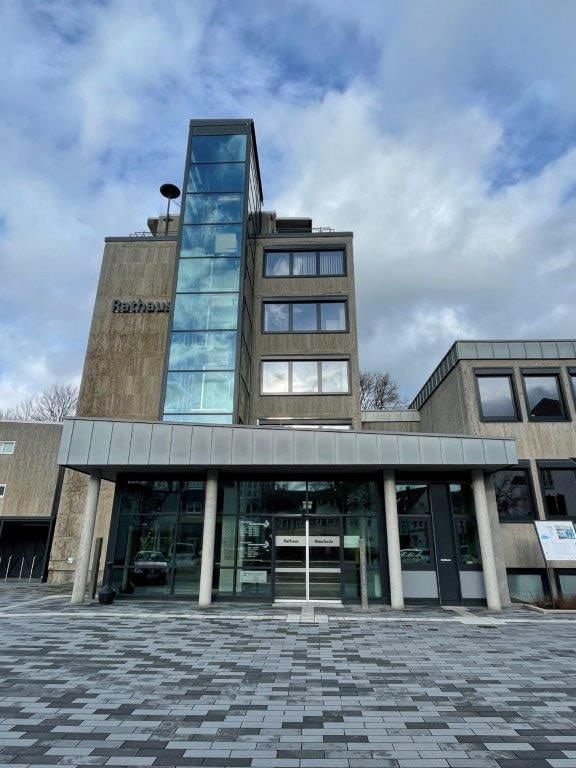 Rathausgebäude mit Glasfassade und Säuleneingang, bewölkter Himmel im Hintergrund.